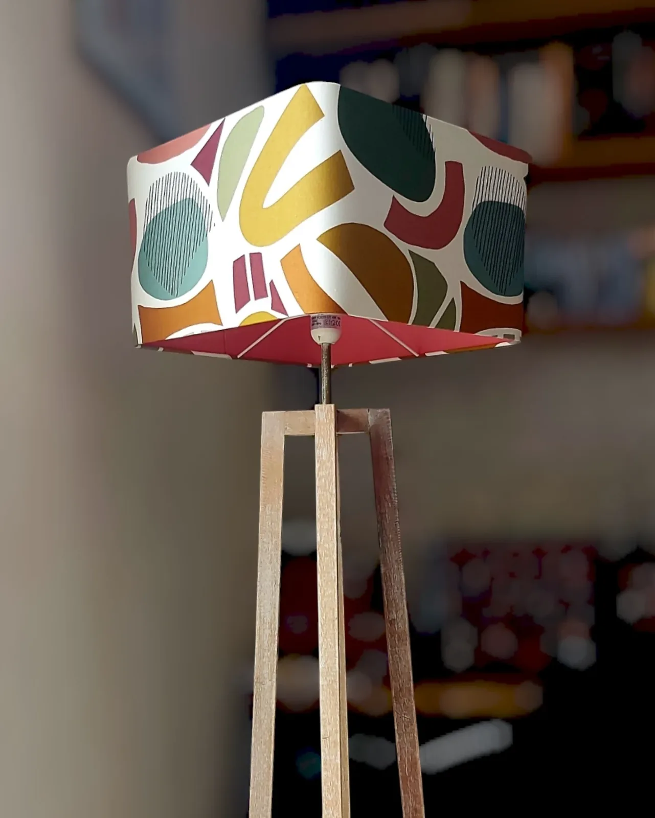Abat-jour carré à motif graphique vert, rouille et jaune sur un lampadaire trépied en bois
