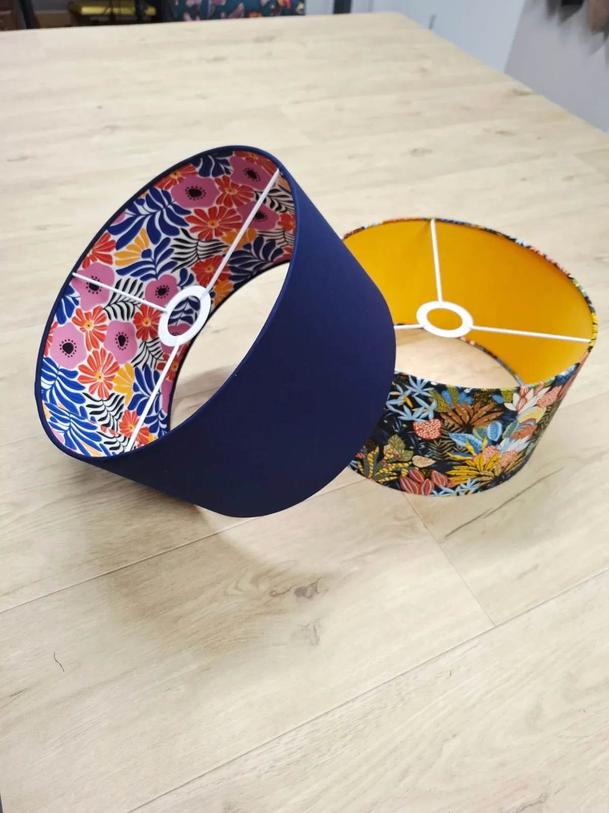 Deux abat-jour tambours bleu marine à l'intérieur fleuri et doré, posés sur une table en bois clair