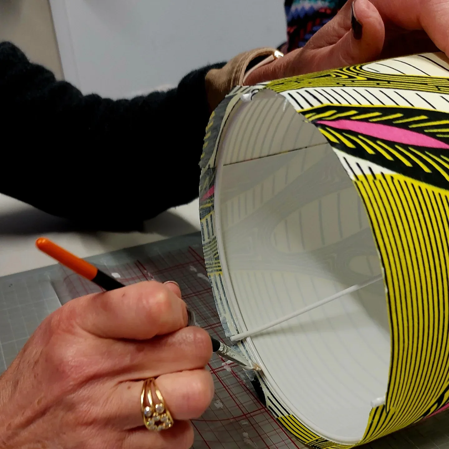 Les mains de Séverine encollant un tissu wax sur un tambour d'abat-jour, avant de remborder