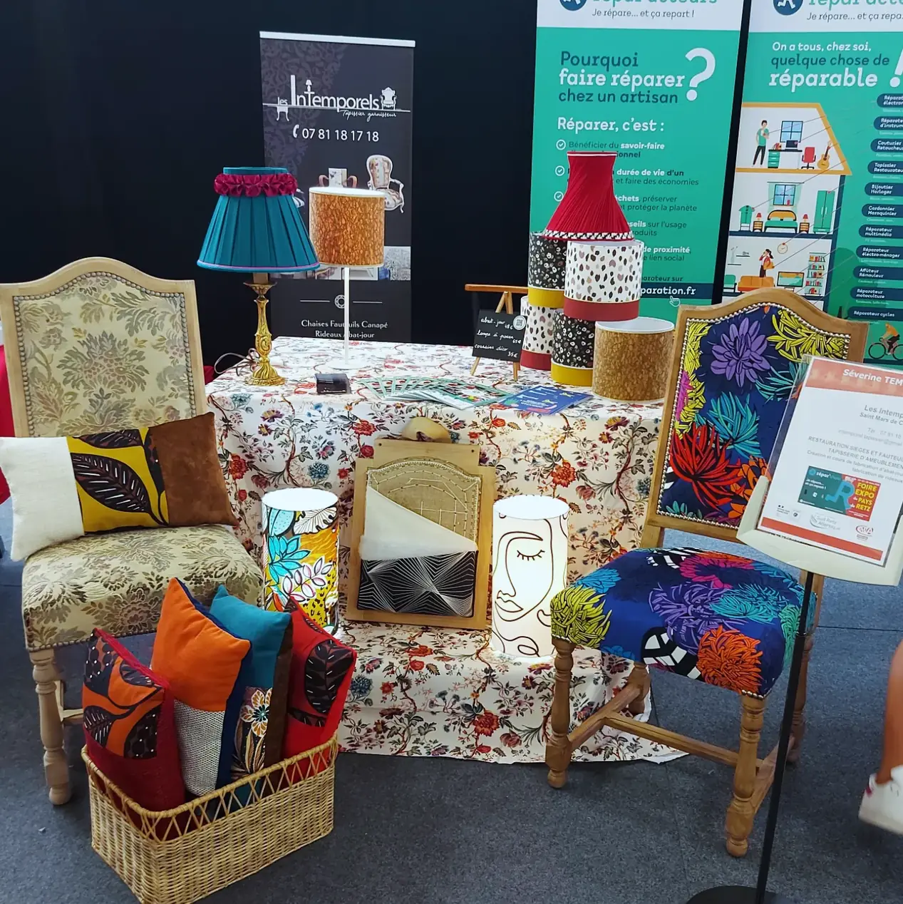 Stand Les Intemporels sur un salon : fauteuils retapissés, coussins et lampes présentés sur une nappe fleurie