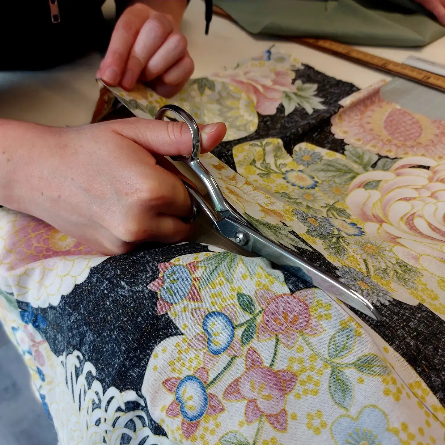 Mains d'une participante coupant aux ciseaux un tissu fleuri sur la table de l'atelier