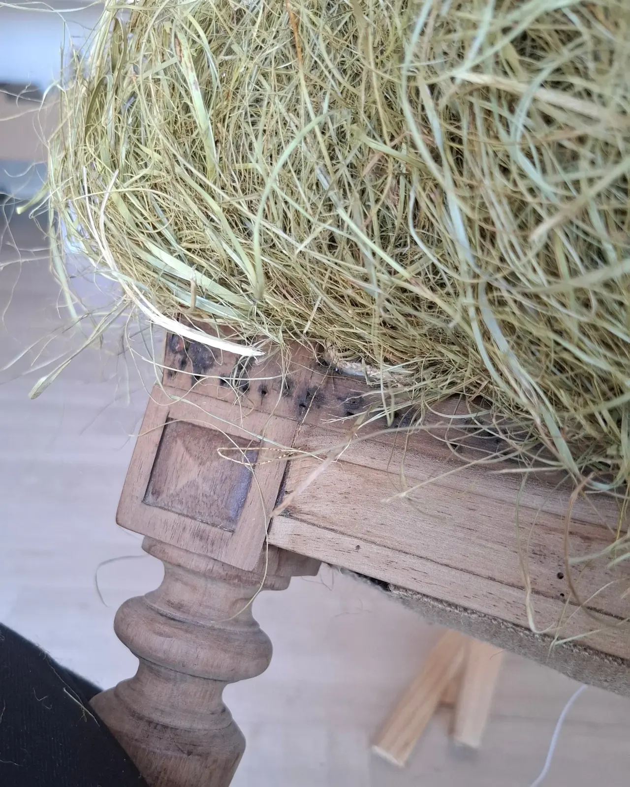 Gros plan sur une poignée de crin végétal posée sur la structure en bois tourné d'un fauteuil