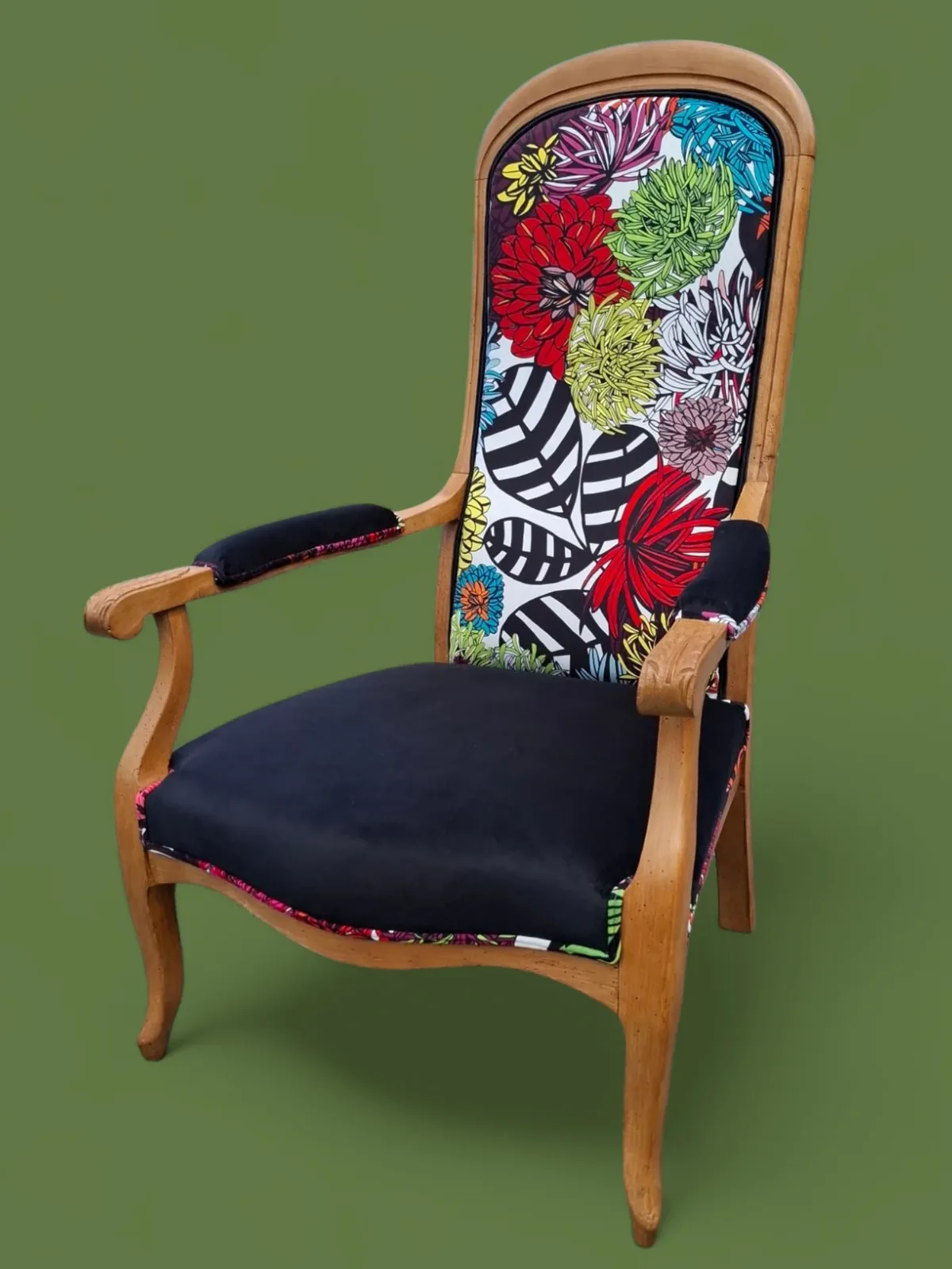 Fauteuil Voltaire retapissé, dossier en tissu fleuri multicolore et assise en velours noir, sur fond vert