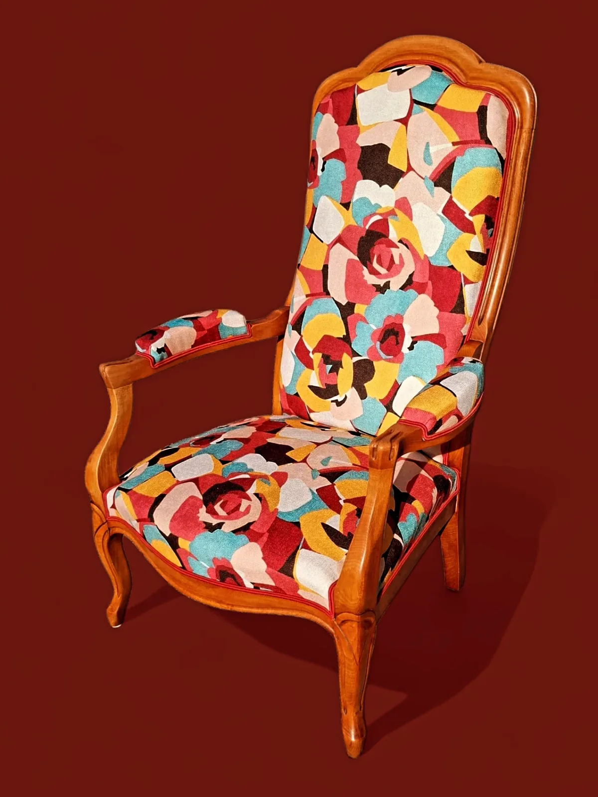 Fauteuil Voltaire retapissé d'un tissu patchwork multicolore, sur fond rouge brique