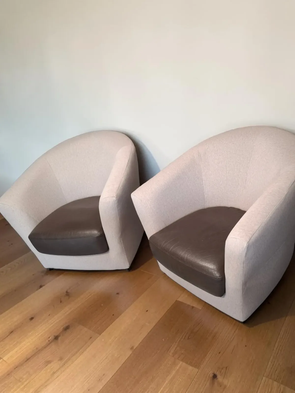 Paire de fauteuils tonneaux retapissés en beige avec coussins simili cuir brun, sur parquet clair