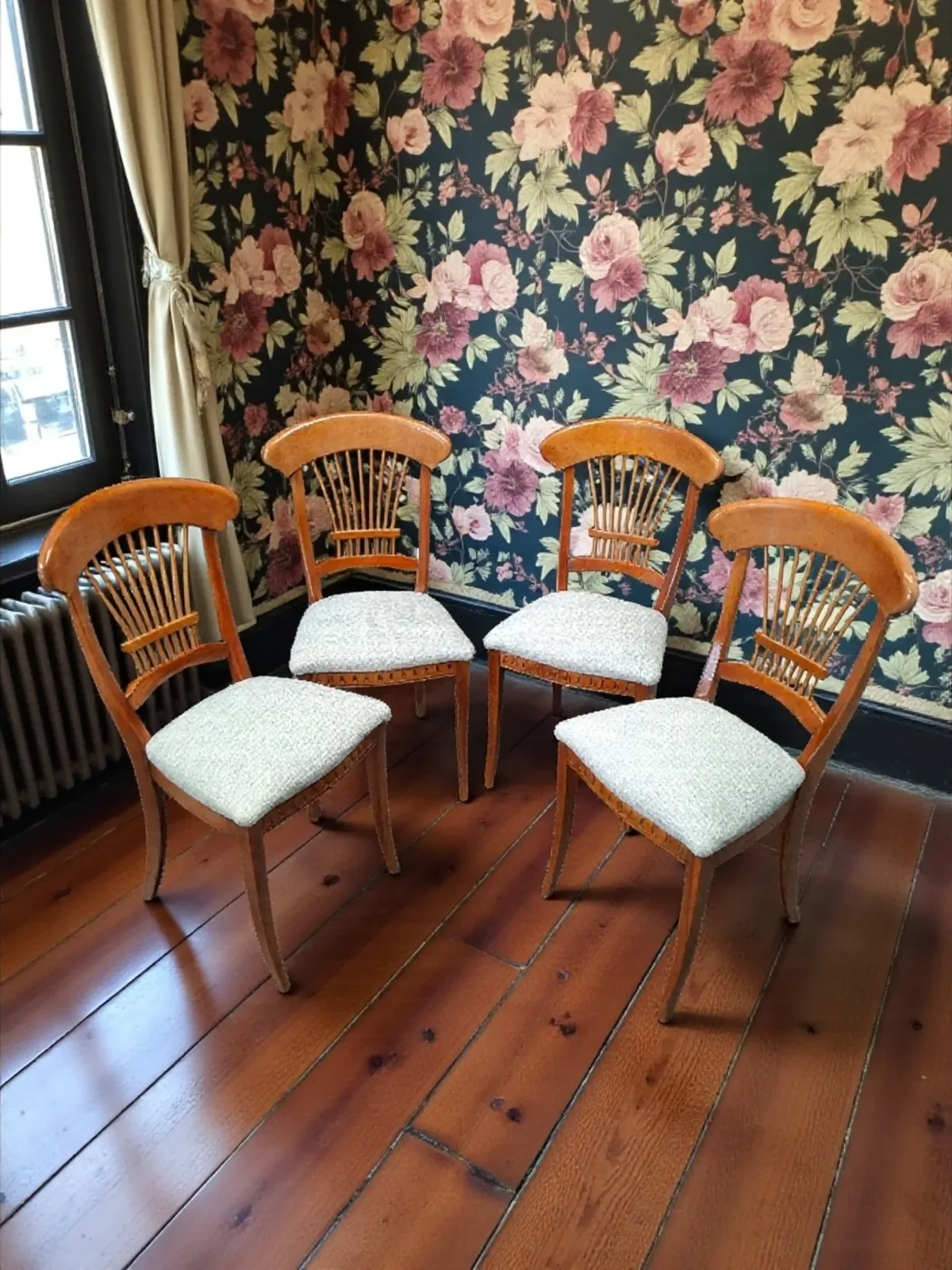 Quatre chaises en bois à barreaux avec assises en tissu chiné bleu clair, devant un papier peint fleuri